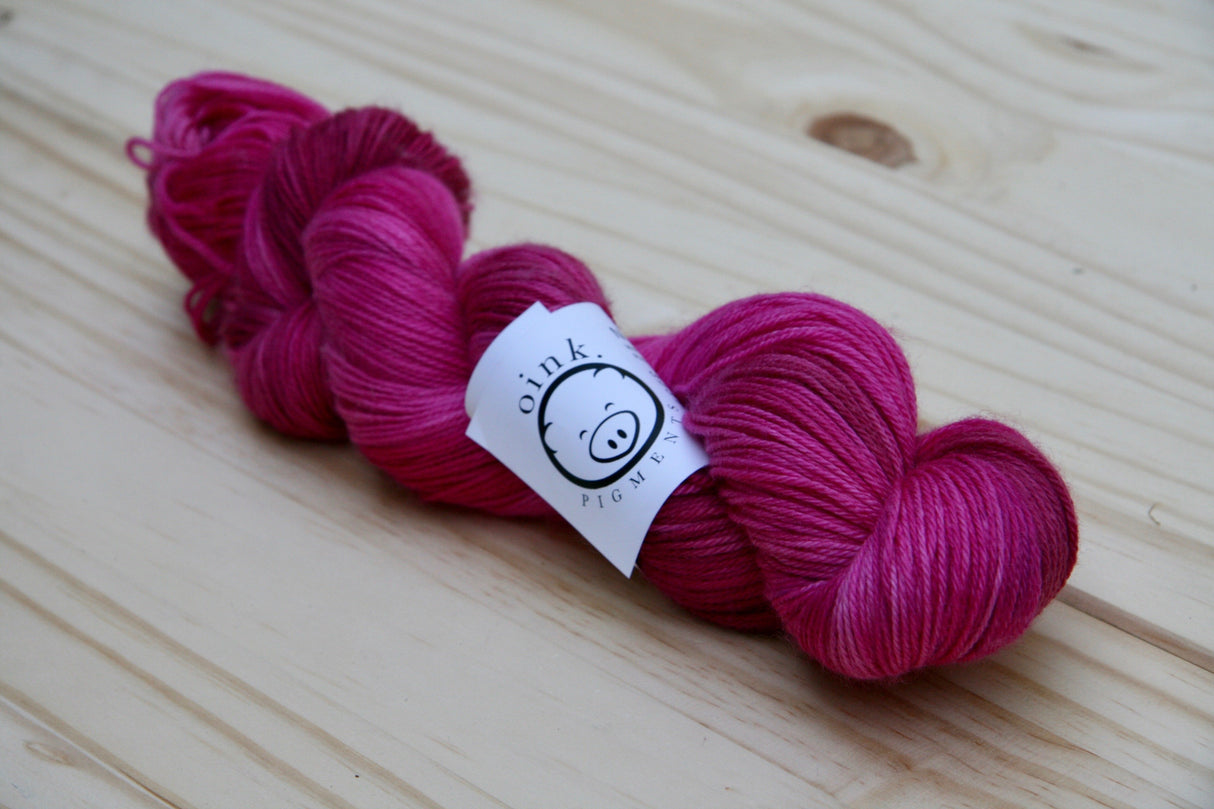 a bright twist of yarn rests against a light wooden background.