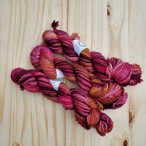 three skeins of brightly colored yarn rest on a light wooden background.