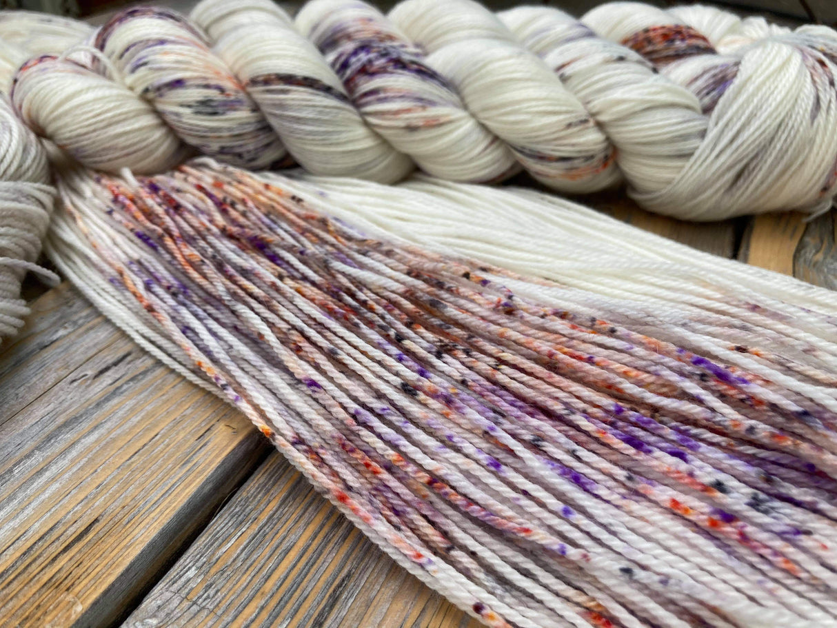A swatch of unhanked yarn lies diagonally across the frame. Another twisted skein rests atop and near the top of the frame. A wooden background can just be seen at the bottom left corner.