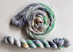 A swirl of yarn sits above a twisted hank on a clean white background.