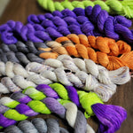 a variety of mini skeins in Halloween colors lay jumbled on a dark wooden table.