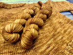 Two skeins of yarn rest diagonally in the frame atop a knitted sweater in the same colorway. 