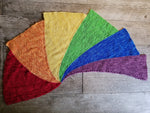 A bright rainbow of colors, in six garter stitch wedges, sits atop a wooden background. 