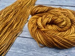 a swath of flat yarn sits on a wooden background with a swirling skein of yarn resting to the right.