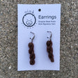 miniature skeins of yarn dangle from steel earring hooks on a white card with the Oink Pigments logo and information at the top.