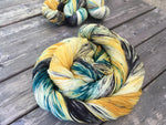 A colorful swirl of yarn curls around itself while three twisted skeins rest in the upper right corner.  The yarn is various deep yellow and green tones. 