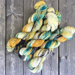 Three twists of yarn rest on a grey wooden backdrop.  The yarn is green and yellow with smudges of black. 