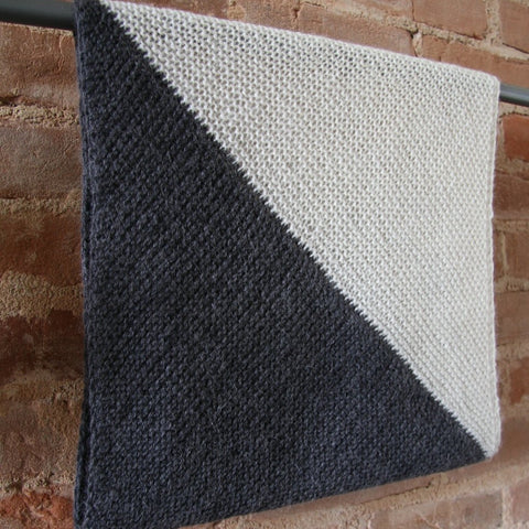 A stunningly simple and bold pair of triangles form a cowl that rests against a brick background.