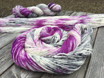 A swirl of yarn rests in the foreground while two more skeins (one laid flat and one twisted) rest in the background.  The yarn is sitting on a grey wooden background.