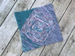 A cowl made of garter triangles in a variety of colors rests on a pale wooden background.