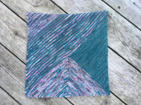 A cowl made of garter triangles in a variety of colors rests on a pale wooden background.