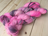 Two skeins of pink and grey yarn rest against a wooden background. 