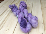 Two skeins of dappled purple yarn rests against a light wooden background.