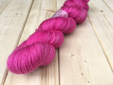 a bright twisted skein of yarn rests on a light wooden background. 
