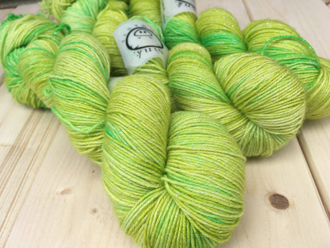 Three bright skeins with subtle sparkle snuggle on a pale wooden background.