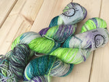Two skeins of yarn rest diagonally in the frame against a wooden background. 4-Play colorway in disco base.