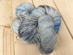 A skein of yarn with subtle sparkles running through it rests against a light wooden background. 