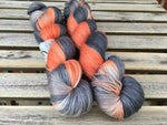Two skeins of orange and grey yarn rest against a wooden background. 
