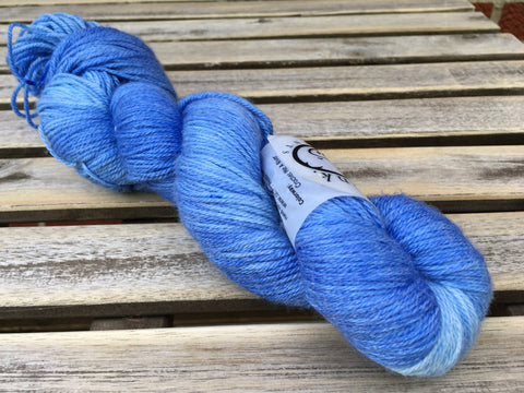 a skein of deep blue with lighter blue tones rests on a light wooden background. 
