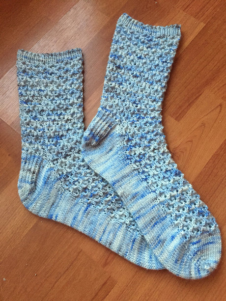 Two handknit socks lie prettily on a wooden floor. 