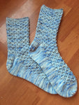 Two handknit socks lie prettily on a wooden floor. 