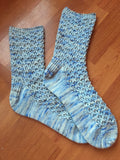 Two handknit socks lie prettily on a wooden floor. 