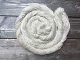A softly shimmery yarn rests in a swirl against a dark wooden background. 