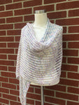 A lacy wrap twirls around the shoulders of a torso mannequin against a brick background. 