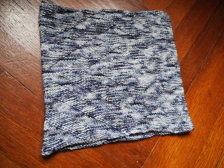 A cowl with a textural herringbone pattern rests against a herringbone patterned wooden floor.