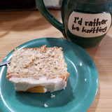 A slice of something delicious sits on a blue plate with a mug in the upper right hand corner says "I'd rather be knitting"