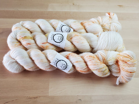 Three pale skeins of yarn with a light sprinkle of yellows and oranges, rest on a wooden background.