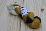 A twisted skein of honey yellow, black, and white rests against a pale wooden background. 