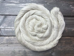 A luminously pale swirl of yarn rests atop a dark wooden background. 