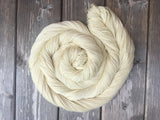 A swirl of pale cream yarn rests on a dark wooden background. 