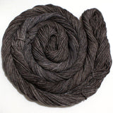 A richly toned swirl of dark brown yarn rests against a clean white background. 