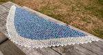 An image of the wingspan and general shape of the shawl as it rests on a well loved picnic table.  Brown-green grass is visible in the upper right corner of the frame. 