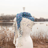 An image of the Bonfire Shawl wrapped around the shoulders of a white mannequin against a brown & silver lakeside background. 