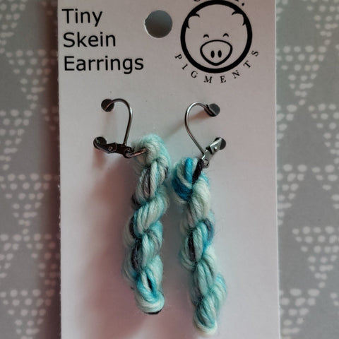 miniature skeins of yarn dangle from steel earring hooks on a white card with the Oink Pigments logo and information at the top.
