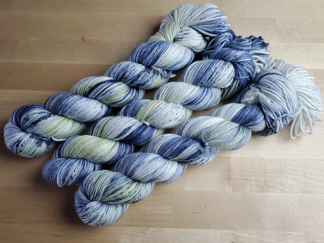 Three skeins of yarn snuggle against a light wooden background. 