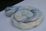A swirl of pale cream and soft blue yarn rests on a clean white background. 
