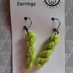 Dill-icious green miniature skeins of yarn dangle from steel earring hooks on a white card with the Oink Pigments logo and information at the top.