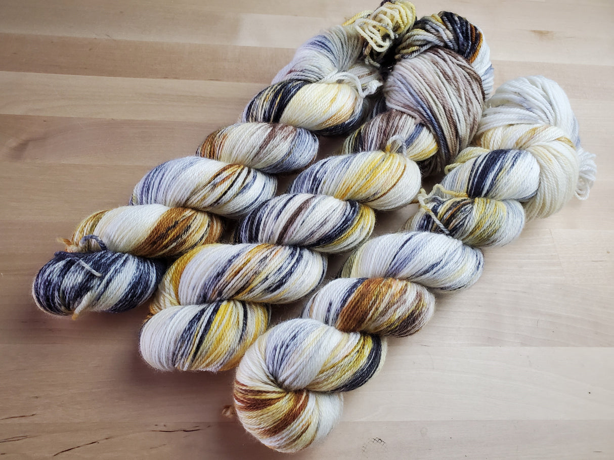 Three skeins of yarn snuggle against a light wooden background. 