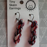 miniature skeins of yarn dangle from steel earring hooks on a white card with the Oink Pigments logo and information at the top.