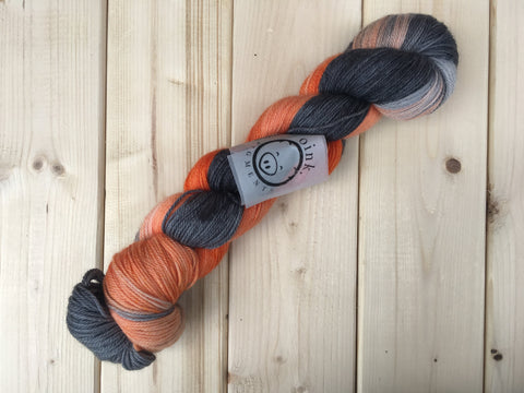 A twisted skein of orange and black-grey yarn lies against a light wooden background. 