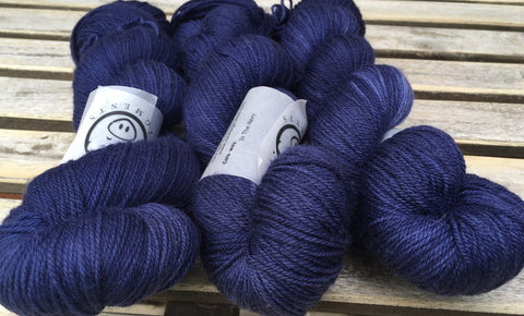 Three skeins of incredibly deep navy blue snuggle together on a wooden background.