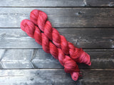 Two skeins of yarn snuggle on a rustic looking wooden background.
