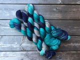 Three skeins of yarn in shades of teal, navy, and grey snuggle against a dark wooden background. 