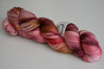 A skein of intense scarlet, deep antique gold and soft pink rests diagonally on a white background. 
