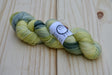 A twisted skein of lemony yellow, black, and grey rests against a pale wooden background. 