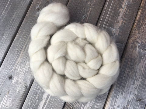 A fluffy braid of undyed fiber rests on a wooden background.